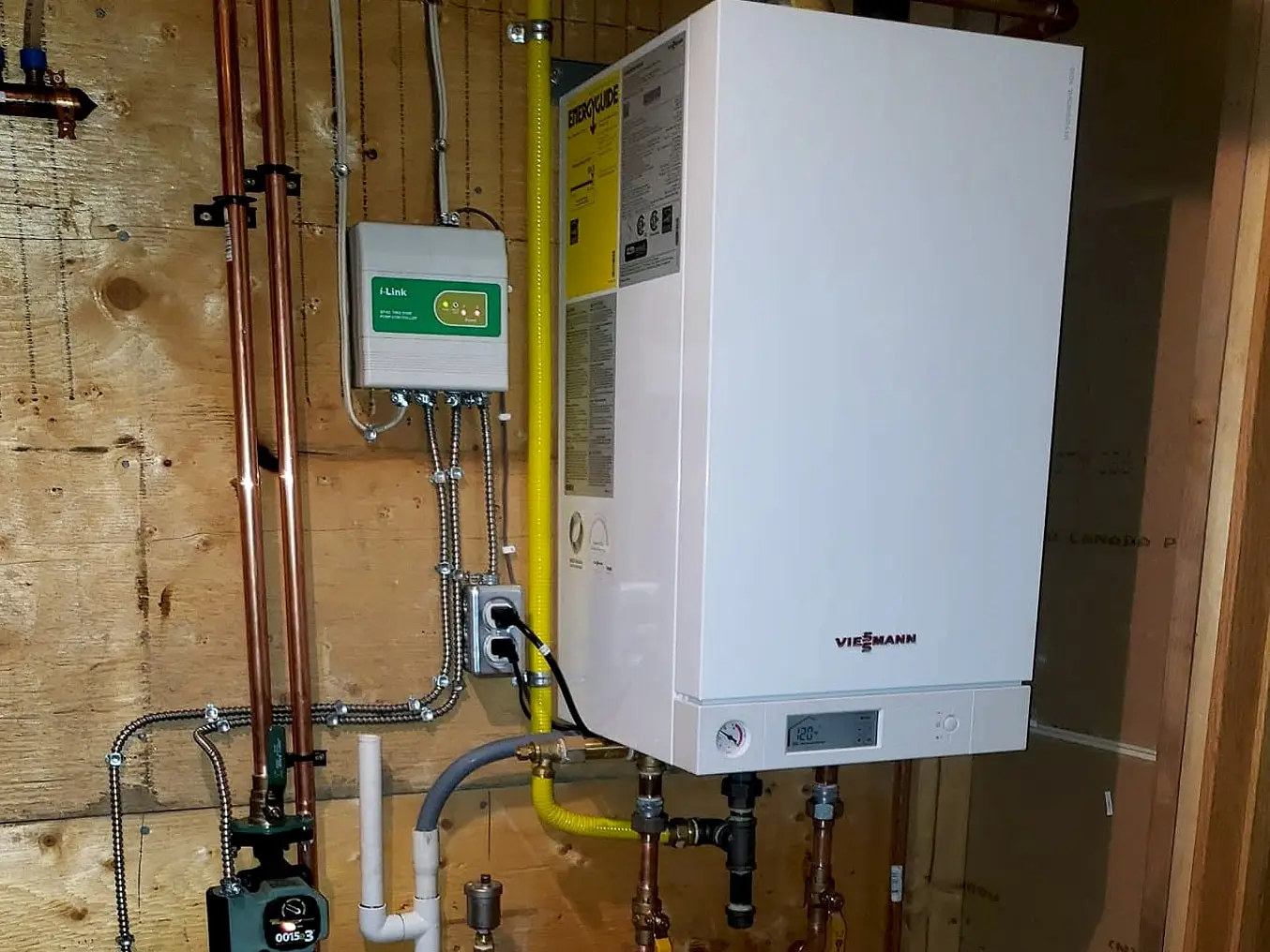 Wall-mounted high-efficiency boiler with copper near-boiler piping, circulator pumps and expansion tank on a plywood wall