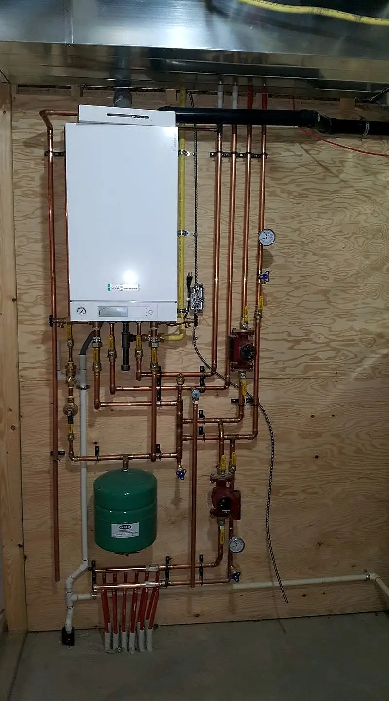 Wall-hung boiler with copper piping, circulator pumps and red in-floor heating loops feeding into a manifold
