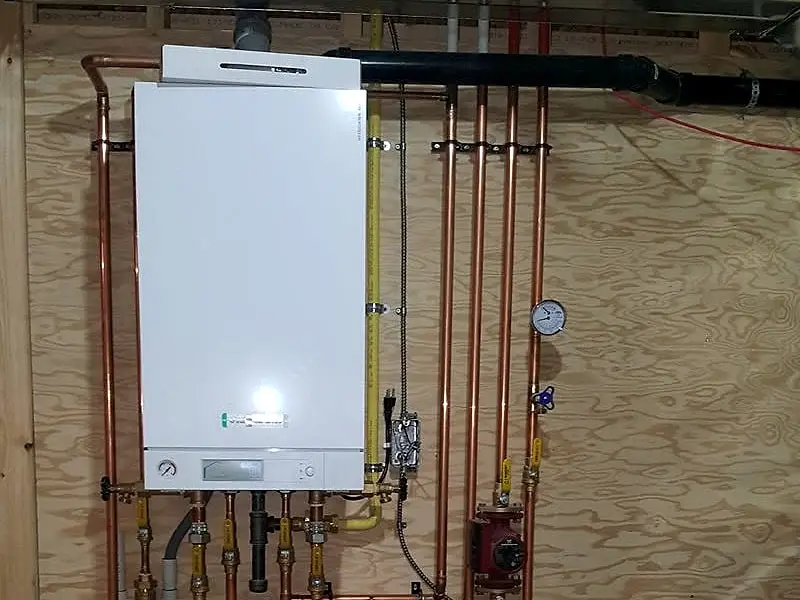 Wall-hung boiler with copper piping, circulator pumps and red in-floor heating loops feeding into a manifold