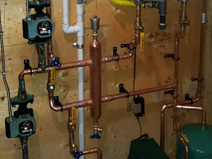 Close-up of copper heating pipes with two circulator pumps, ball valves and a vertical copper header on a plywood wall
